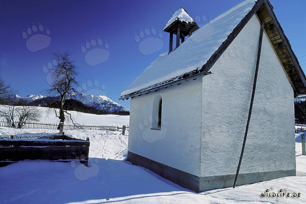 Atmospheric winter landscape with a snow-covered chapel in Bavaria