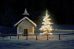 Festive Christmas Atmosphere with Old Chapel and Illuminated Christmas Tree in Snowy Mountains